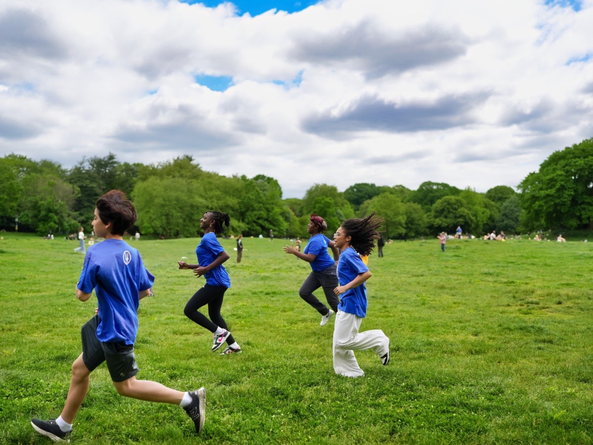 Run4Fun runners in blue shirts running across the meadow in Prospect Park